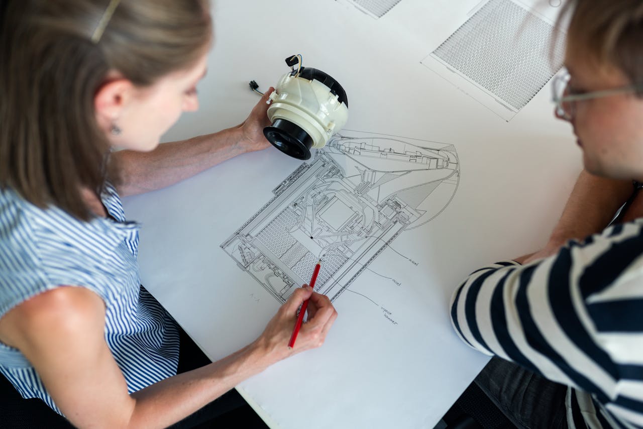 Two engineers collaborate over a detailed technical design blueprint, focusing on innovation and planning.